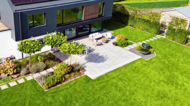 Vue aérienne d'un jardin moderne avec une terrasse, des meubles de jardin, des pelouses et des parterres de fleurs.