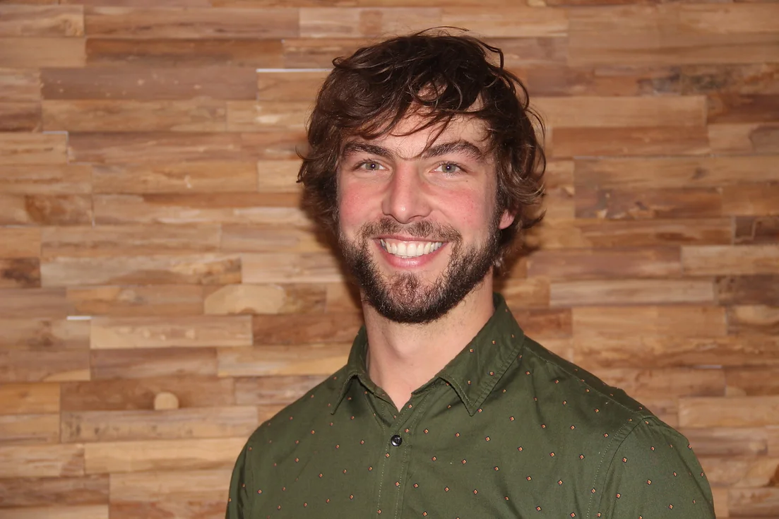 Photo de Jérémy Nique, gérant de l'entreprise, souriant devant un fond en bois.